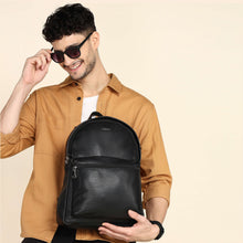 Load image into Gallery viewer, A man wearing a brown shirt is holding a black genuine leather backpack with shoulder straps and a grab handle.