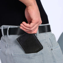 Load image into Gallery viewer, Person wearing a Sassora black leather wallet in a gray pocket with a plain background